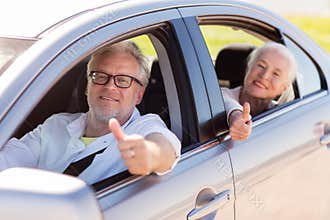 Senior couple driving in car and showing thumbs up