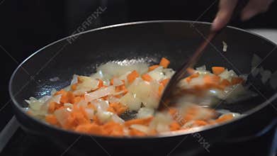 Chopped onions and carrot fried in vegetable oil in the pan. Close-up adding carrot on top of the pan. Onions and carrot