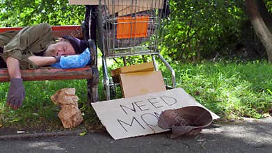 View of drunk homeless man sleeping at day time on the bench in the street.