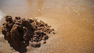Castle on the sand is washed off by a sea wave