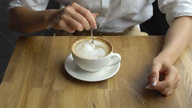 A young beautiful woman drinking coffee in a cafe. Hand of girl stiring sugar in coffee close up