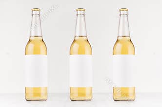 Three transparent longneck beer bottles 500ml with blank white label on white wooden board, mock up.