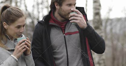 Woman bringing hot beverage or coffee or tea to man in camping place. Couple people in love autumn outdoor trip in