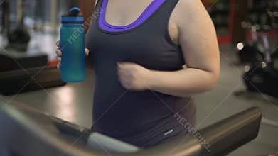 Overweight woman exercising on treadmill, drinking water from bottle, diet