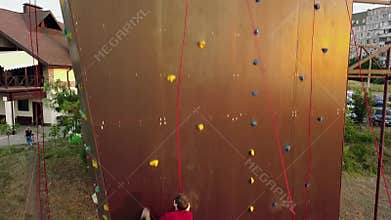 Aerial of climber runs the speed rock climbing track on artificial wall outdoors. Young fast athlete climbs the cliff at