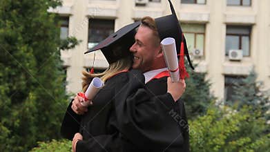 Best friends in academic dresses and hats hugging and smiling on graduation day