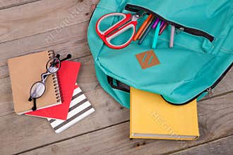 Backpack and school supplies: books, pencils, notepad, felt-tip pens, eyeglasses, scissors on wooden table
