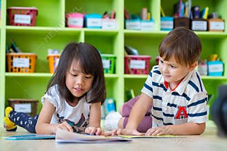 Two kid lay down on floor and reading tale book in preschool lib