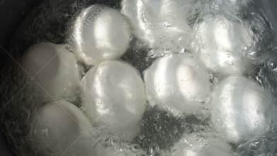 White eggs are boiled in boiling water in a metal pan. One egg cracked. Water boils and bubbles. Close-up, high detail.