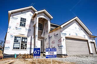 New home partially finished, under construction in residential housing subdivision with for sale sign in yard
