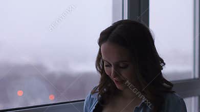 A happy pregnant woman stands at a large panoramic window located at a high altitude. He touches his stomach with his