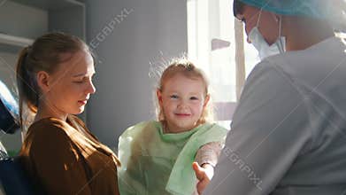 Happy girl with mom in a dental chair at the reception at the dentist