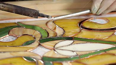 Master is creating a stained-glass panel using soldering iron for fixing
