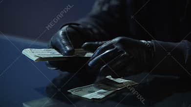 Criminal in black gloves counting bundle of money earned for committing crime