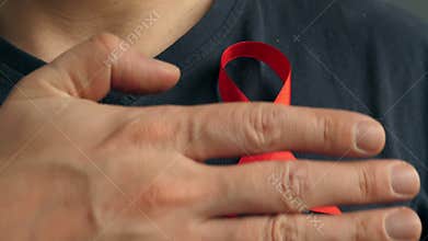 A man attaches a Red awareness ribbon to his shirt. HIV AIDS.