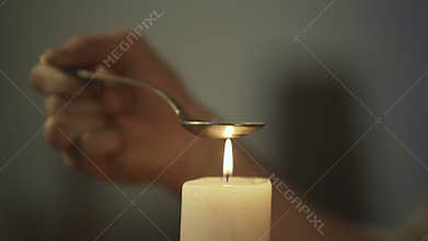 Hand of person heating chemical substance in spoon on candle light, drug abuse