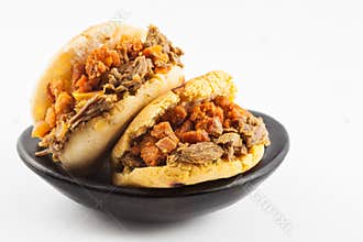 Arepas filled with shredded beef and pork rind served in a black ceramic dish