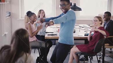 Happy African American businessman enters office, celebrates victory with crazy dance, high-fives colleagues slow motion
