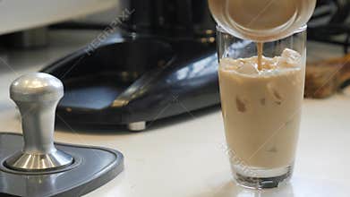 Barista pouring fresh coffee in a glass of ice