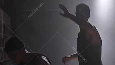 Two basketball players shadow playing one on one indoors in room with smoke and floodlit