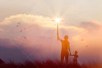 Silhouette of mother and son christian prayers raising cross while praying to the Jesus on sunset background