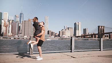 Happy Caucasian man meeting his girlfriend, hugging and smiling at sunny Manhattan skyline in New York City slow motion.