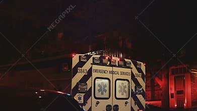 View of rear doors and flashing lights of emergency service ambulance moving away from accident scene at nighttime.