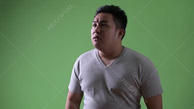 Young handsome overweight Asian man against green background