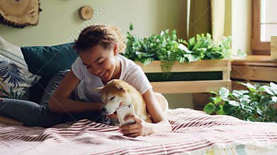 Smiling mixed race teenager is taking selfie with puppy then talking to it and showing it photos on smartphone screen
