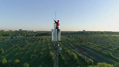 Happy man at work on top of cellular antenna, technician on radio telecommunication tower raises hand with thumb-up on