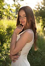 Summer portrait of young beautiful lady wearing long white evening dress posing in the park.