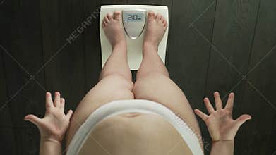 Obese woman standing on bathroom scales, checking weight, anxious, top-view