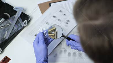 Detective wearing exam gloves, checking bullets from crime scene with magnifier