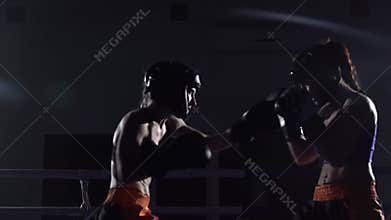 Two girls in helmets box their arms and legs in the ring in the dark. Slow motion