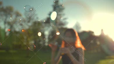 Portrait of beautiful redhair young woman. Blowing bubble in the park