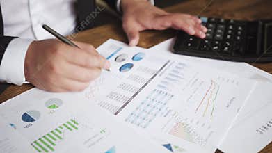 Close up of a businessman hands with pen working at office desk and analyzing graphs and charts and writing a business