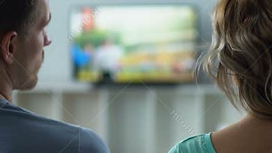 Boyfriend and girlfriend watching TV at home, switching channels, back view