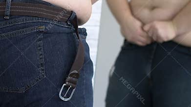 Obese young man trying to put on jeans in shop fitting room, large size, diet