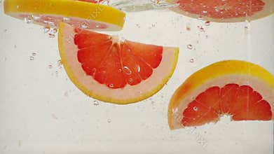 Round grapefruit slices slowly sink in water, slow motion close-up