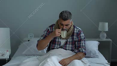 Sick man coughing in bed, drinking antipyretic tea to treat fever, flu epidemic