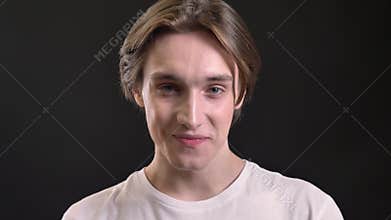 Charming young man looking in camera and laughing, black background, male model with blue eyes smiling