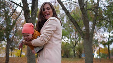 Mom and child playing together in autumn park, family having fun on background trees