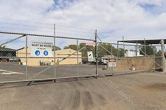 Multiple safety and security warning signs, including hazardous chemicals, on the barbed wire fence of an industrial business site