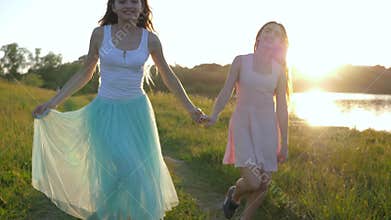 Happy girls teenagers run holding hands along meadow