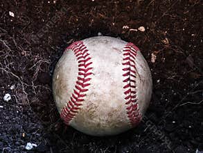 Close up sports background image of an old used weathered leather baseball laying in a pile of brown dirt showing intricate