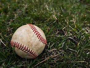 Close up sports background image of an old used weathered leather baseball ball laying in the grass field outside showing
