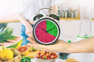 Hand holding a clock in a kitchen. Intermittent fasting concept.  Empty copy space