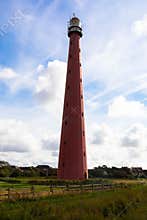 Red lighthouse in the harbor village den Helder against blue sky with cumulus clouds.
