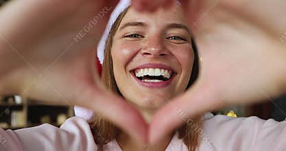 Young lady celebrate Christmas look at camera through finger heart