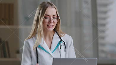 Female nurse caucasian woman medical assistant in glasses video calling distant patient on laptop. Doctor girl therapist